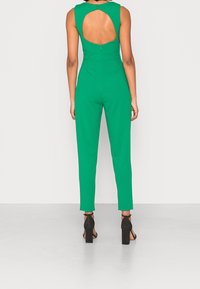 Green jumpsuit with a sleeveless design, open back, and zip closure. Made of smooth fabric, fitted at the waist and straight-leg.