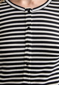 Mustvalge triibuline topp ümarate kaelustega, millel on ees viis musta nuppu ja pehme, elastne kangas.