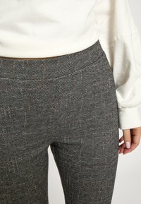 Čierne a sivé nohavice so vzorom a hladkou textúrou, zdobené tenkými nepravidelnými medenými čiarami, s vysokým pásom a priliehavým strihom.