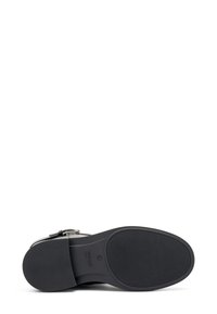 Zapato de cuero negro con una parte superior lisa y suela de goma texturizada, que presenta una hebilla lateral y un diseño de punta redonda.