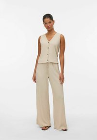 Lichtbeige, getextureerd tweedelig outfit met een mouwloze top met een v-hals en knopen, gecombineerd met brede, drawstring broeken.