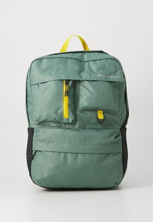 Sac à dos Columbia vert avec plusieurs poches frontales, deux tirettes de fermeture éclair jaunes et une poignée supérieure jaune sur fond blanc.