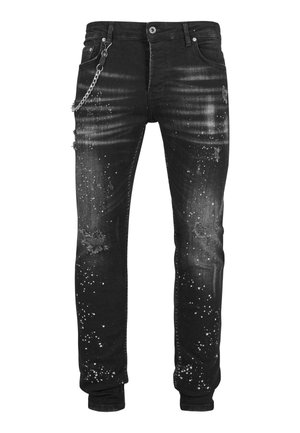 Jeans negros desgastados con un ajuste skinny. Presentan un patrón de salpicaduras, desvanecimiento, detalles rasgados y un acento de cadena plateada en el bolsillo.