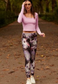 Šviesiai violetinė ilgomis rankovėmis palaidinė, derinama su aukštu liemeniu kelnėmis, turinčiomis daugiakampį abstraktų raštą rožinėmis, pilkomis ir juodomis spalvomis.