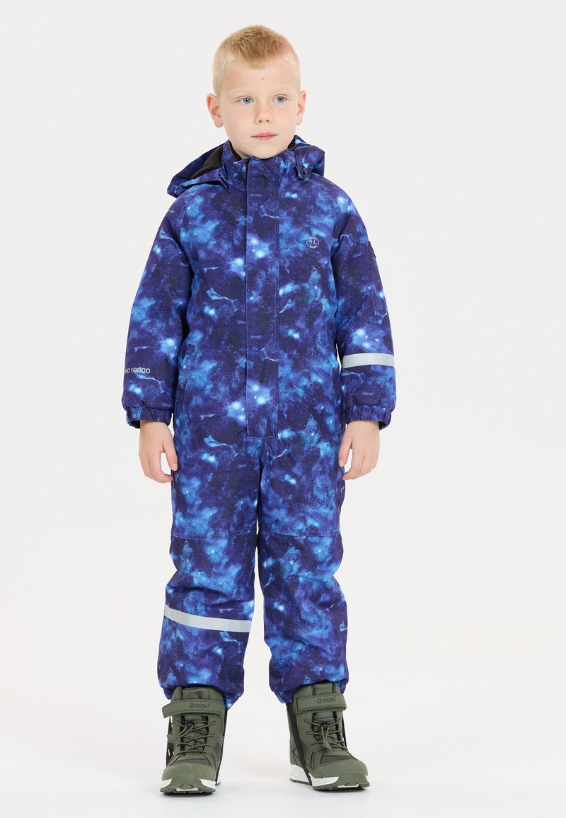 Lilla og blå galaxemønstret børnesnejsuit med reflekterende detaljer, vandtæt stof og en aftagelig hætte. Båret med grønne sneboots.