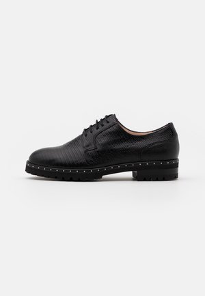 Chaussure en cuir noir avec une finition texturée, bout rond, design à lacets et semelle cloutée. Dispose d'une semelle extérieure robuste pour une meilleure adhérence.