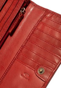 Portefeuille en cuir rouge avec des compartiments zippés, plusieurs emplacements pour cartes et une fermeture à bouton pression avec un logo embossé à l'intérieur.