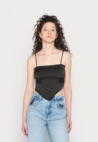 Camisola de cetim preta com alças finas e uma bainha triangular, combinada com jeans de ganga de cintura alta em azul claro.