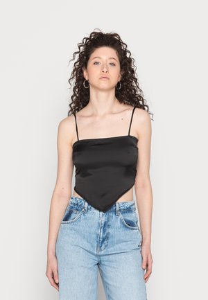 Camisola de cetim preta com alças finas e uma bainha triangular, combinada com jeans de ganga de cintura alta em azul claro.