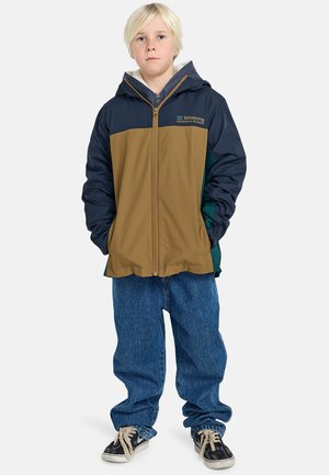 Giacca con cappuccio marrone, blu e verde, con zip frontale, polsini elasticizzati e logo Billabong. Indossata su jeans blu larghi e sneakers.