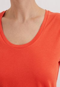 Czerwona bawełniana koszulka z okrągłym dekoltem i krótkimi rękawami, gładka w dotyku, o prostym designie bez wzorów i ozdób.