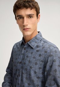 Gestreept overhemd met een geometrisch ontwerp in verschillende tinten blauw en zwart. Gemaakt van lichte stof met een klassieke kraag.