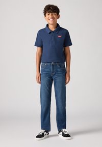 Μπλέ πόλο μπλούζα με λογότυπο Levi's, σε συνδυασμό με μπλε τζιν παντελόνι. Το μοντέλο φοράει μαύρα και άσπρα sneakers. Απλό, περιστασιακό ντύσιμο.