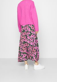 Pull rose oversize associé à une jupe longue fleurie avec de grandes fleurs roses sur fond vert, complété par des baskets blanches.