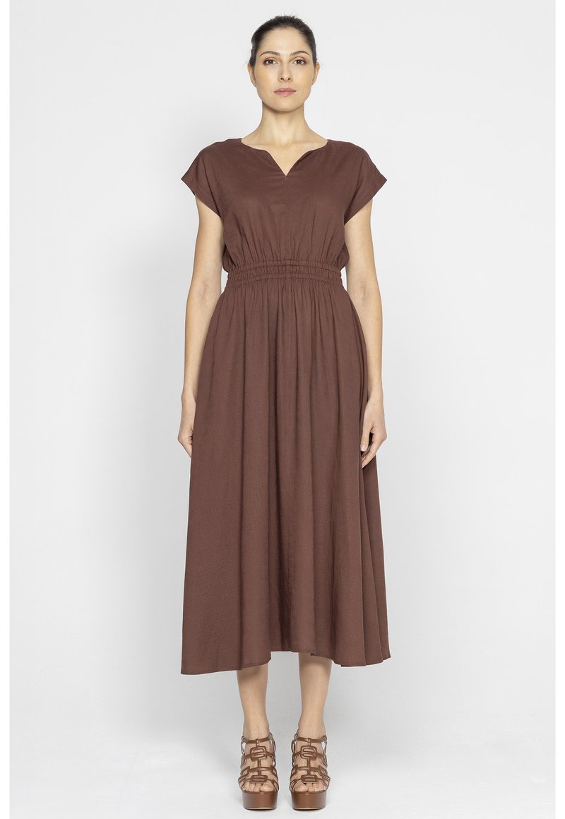 Brązowa sukienka do kolan z krótkimi rękawami, dekoltem w kształcie litery V i elastycznym pasem. Charakteryzuje się zwiewnym krojem i gładką fakturą. Połączona z brązowymi sandałami na paski.