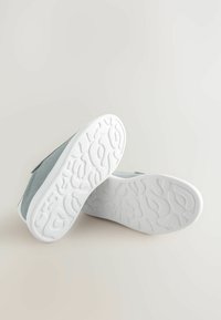 Grå ruskindsko med en hvid tekstureret gummisål. Hælene er let forhøjede; den overordnede form er rund med et simpelt design.