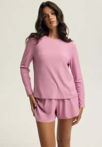 Różowy, prążkowany zestaw odzieży domowej z długim rękawem i dopasowanymi szortami. Miękka tekstura, luźny krój i minimalistyczny design.