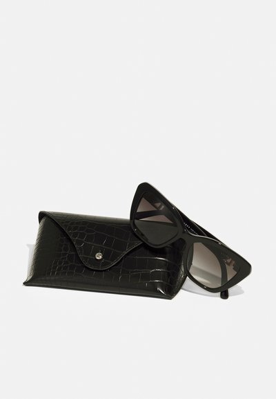 Ochelari de soare negri cu un cadru unghiular și lentile degradate, așezați lângă un etui negru cu model de crocodil, având un sistem de închidere cu buton.