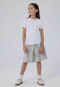 T-shirt bianco a maniche corte abbinato a pantaloni corti grigio chiaro con motivo a serpente, caratterizzati da una vestibilità ampia e un taglio a lunghezza ginocchio. Abbinato a sneakers bianche.