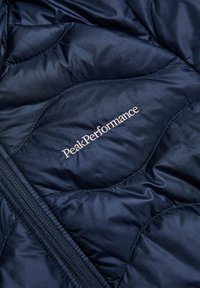 Marineblaue Daunenjacke mit gestepptem Muster, subtiler Oberfläche und dem in silbernem Faden gestickten "Peak Performance"-Logo. Mit Reißverschluss.
