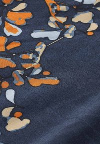 Mörkt tyg med ett abstrakt mönster av orange, grå och beige former, med en texturerad yta och en slät finish.