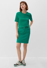 T-shirt en coton vert à manches courtes associé à une jupe en denim verte. La tenue présente un design simple et des sneakers décontractés avec des accents.