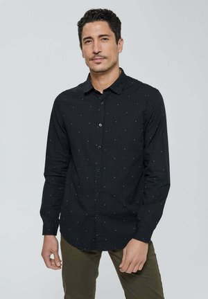 Chemise noire à boutons, avec un motif de points subtil, manches longues, col pointu et un tissu lisse et texturé.