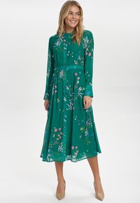 Hossz�ú zöld ingruha, könnyű anyagból készült, színes virágmintával, gombos záródással és hosszú ujjakkal, övvel kiegészítve.