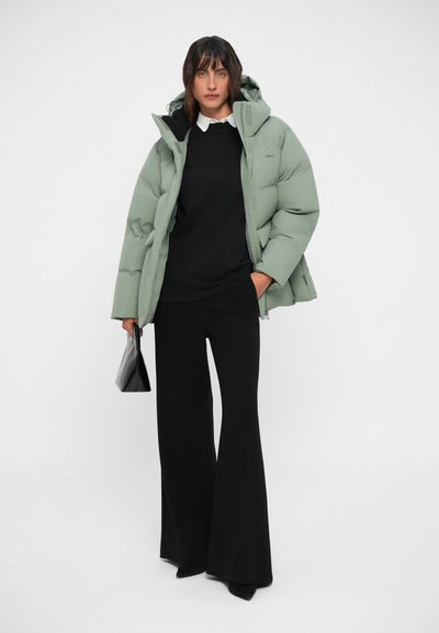 Light green puffer jacket with a hood, black top, and flared black pants. The outfit also includes a small black handbag.