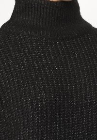Maglione nero con collo alto lavorato a maglia, realizzato in un tessuto morbido e testurizzato. Presenta un colletto a coste e leggere sfumature di colore chiaro sparse in tutto il capo.