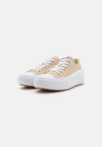 Beige canvas sneakers met witte rubberen zolen en neuzen, voorzien van witte veters en een unieke gelaagde platformontwerp.