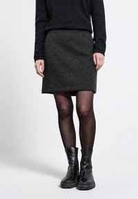 Harmaa villahame, jossa on suora leikkaus, käytettuna mustien läpinäkymättömien legginsien ja mustien nilkkabootsien kanssa. Asusteessa on yksinkertainen ja siisti muotoilu.