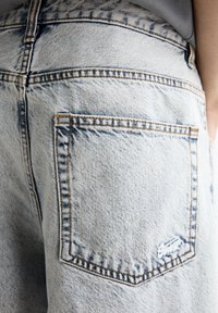 Pantalones cortos de mezclilla azul claro con un bolsillo trasero, costuras visibles y textura deslavada. La tela muestra un ligero desgaste y un sutil efecto de arrugado.