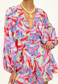 Blouse colorée à motif floral avec encolure à volants, manches bouffantes et short assorti. Collier de perles jaunes avec un pendentif en forme de citron.