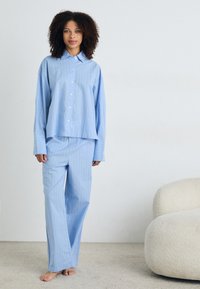Ljusblå, randig pyjamas med knappar som har en avslappnad passform. Långa ärmar och vida byxor gjorda av mjukt tyg, med minimal detaljering.