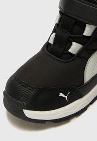 Scarpa sportiva nera con tomaia sintetica testurizzata, dettagli grigi a contrasto, fasce regolabili e suola in gomma con logo bianco.