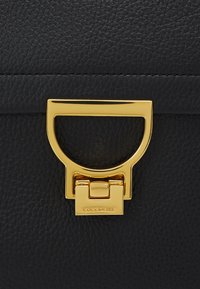 Borsa a mano in pelle nera con chiusura in metallo dorato con un ritaglio arrotondato e logo inciso. La superficie ha una finitura testurizzata.