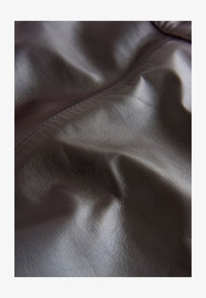 Brunt læderstof med en glat, tekstureret overflade med subtile folder og en ensartet glans. Syningen er minimal og diskret.