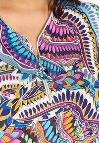 Blusa a fantasia astratta colorata con una cerniera argentata e un tirazip a forma di foglia blu nella zona della clavicola.