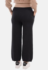 Pantaloni neri a gamba larga in tessuto morbido, con tasche laterali e vestibilità rilassata, abbinati a sneakers bianche con logo nero.