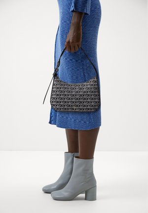 Černobílá ramenní taška s potiskem loga a zakřiveným tvarem, doplněná o modré žebrované šaty s texturou a světle šedé kotníkové boty na podpatku.