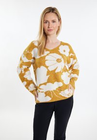 Sweter w kształcie V w musztardowym kolorze z białym wzorem kwiatowym. Wykonany z miękkiego materiału, z długimi rękawami i bocznymi kieszeniami.