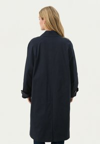 Námořnický modrý trenčkot vyrobený z odolné látky, s zadním yoke, dlouhými rukávy s knoflíkovými detaily a rovnou siluetou.