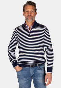 Marineblauw en witte gestreepte pullover van een zachte breimateriaal, met een ritskraag en geribde manchetten. Gecombineerd met blauwe jeans.