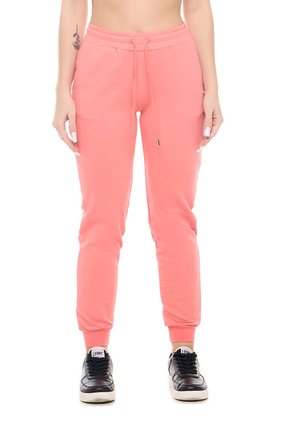 Un mannequin cadré partiellement porte un pantalon de jogging rose corail à cordon de serrage et à chevilles resserrées, ainsi que des baskets noires sur fond blanc.