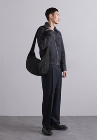 Giacca in denim nera con zip, pantaloni neri larghi e una borsa a tracolla nera. Le scarpe nere completano l'outfit. Sfondo neutro.