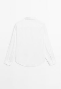 Camicia bianca a maniche lunghe, con colletto classico, dettagli con bottone ai polsini e un tessuto leggero e liscio con orlo curvo.