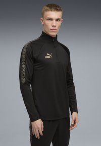 Svart långärmad träningströja med hög krage. Har guldlogotyp, texturerade mönstrade axelaccenter och en slim fit design.