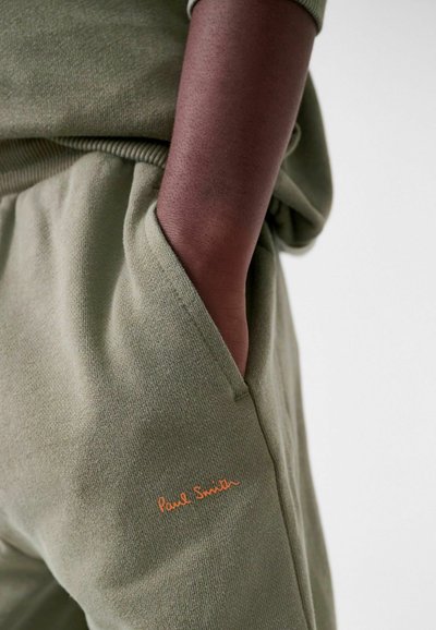Olivengrønne sweatpants med en blød tekstur, med et orange "Paul Smith" logo broderet på lommen. Modellen har hånden i lommen.