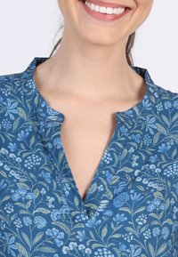 Blaues Blumenshirt aus einem weichen Stoff, mit einem V-Ausschnitt und aufwendigen botanischen Mustern in Hellblau und Grün auf einem dunkelblauen Hintergrund.